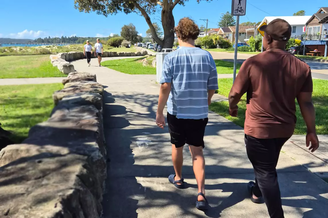 A young disabled man is walking alongside the beach with his support provider